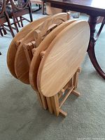 Image of four oval wooden TV tray tables folded and stored upright in a wooden rack, showing the tops and side profiles.