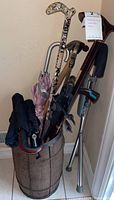 Wooden barrel umbrella stand holding various walking canes and umbrellas