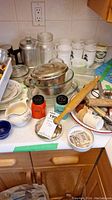 Wide view of vintage kitchen items on counter including ceramic cream and sugar set, glassware, rolling pin, salt and pepper shakers, and metal percolator.
