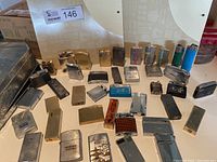 Overview of 28 assorted metal lighters arranged on white surface