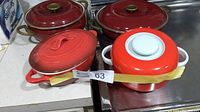 Four casserole cookware pieces: two deep red Copco cast iron casserole pans with lids, one red ceramic casserole with lid, and one small cream ceramic casserole dish without lid visible.
