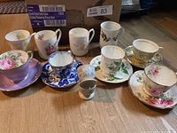 Overview of the collection of china teacups, saucers, and mugs arranged on the floor showing variety of patterns, colors, and styles