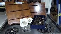 Two wooden wall racks for holding miniature souvenir spoons, a blue box containing assorted silver miniature spoons and utensils, and two small decorative royal collector plates laid out on a stove top.