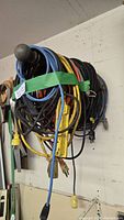 Side view showing various colored extension cords coiled and hanging on hook, with different sizes and plugs visible, bound with green tape.