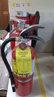 Photo showing front view of 3 red fire extinguishers with metal handles and hoses.