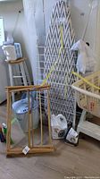 Photo showing ironing board, wooden drying rack, metal drying rack, bucket, black and decker iron and gallon container on floor