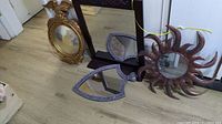 Four decorative mirrors arranged on floor showing varied frame styles and finishes