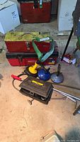 Photo showing two red metal toolboxes, one black plastic case, and three manual drain clearing tools with yellow and blue handles on the floor.