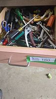 Drawer filled with assorted hand tools including scissors, screwdrivers, pliers, wrench, and other items.