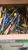 Drawer full of assorted hand tools such as wrenches, screwdrivers, pliers, and other general hand tools with different handle colors and conditions.