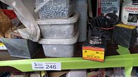 Photo showing three large stacked plastic bins filled with metal screws and nails. A metal dish and a small box of casters are visible on the shelf.