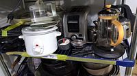 Shelf view showing several kitchen appliances including white crock pots, toaster, coffee press, and waffle press