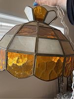 Close-up image showing stained glass hanging lamp with amber, white, and textured brown glass panels in a metallic frame.