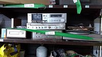 Shelf view of stereo equipment including Hitachi receiver and Kenwood amplifier.