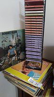 Metal rack holding over 30 self-help CDs in various colored jewel cases with some vinyl record covers visible next to the rack including Robert Klein