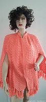 Full front view of vintage orange knit cape on mannequin showing textured zigzag pattern and tassels.