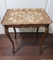 Front view of vintage Florentine style end table showing scalloped composite top with floral and scroll design and curved carved wooden legs.