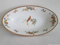 Top-down image showing entire oval dish with golden pheasant in center, floral border, and gilt rim design.