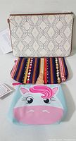 Three zipper pouches stacked: largest white with diamond design, middle southwestern stripe, smallest unicorn design.