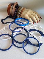 Image showing variety of vintage bangle bracelets in different sizes and colors arranged on and near a mannequin hand, including tortoiseshell, brown, metallic, black, blue, and white bangles.