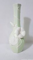 Full front view of the pale green vase showing its tall slender shape and white 3D floral decoration.