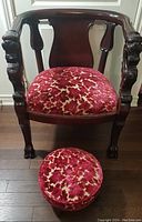 Front view of carved armchair and round footstool showing overall design and upholstery