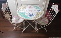 Full view of the 3-piece bistro set including table and two chairs, showing colorful mosaic patterns and wrought iron frames.