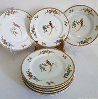 Eight vintage 6-inch porcelain bread plates with golden pheasant and floral pattern arranged on display stands.