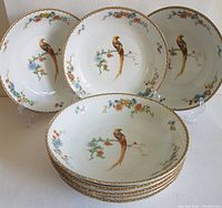 Eight white porcelain coupe bowls with golden pheasant and floral pattern, stacked and displayed on plastic stands.
