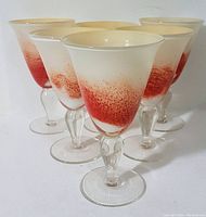 Front angle showing 6 goblets with red splatter pattern on white frosted glass in a staggered formation.