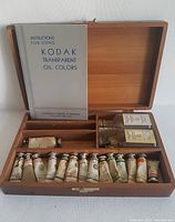 Photo of open wooden box showing the instruction booklet, two glass fluid bottles and multiple metal tubes of oil paint.
