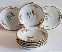 Stack of 8 porcelain nappies featuring golden pheasant and floral pattern with gold trim