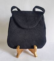 Front view of vintage black Cordé evening bag on a wooden stand, showing textured wave pattern and flap closure.