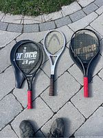 Three tennis racquets laid on paving stones showing front view of racquets and handle grips