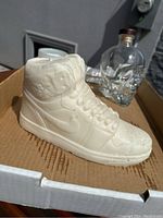 White Air Jordan sneaker-shaped candle with detailed laces and swoosh logo placed inside a cardboard box.