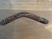 Top side of the wooden boomerang showing painted tribal designs in black, white, yellow, and red.