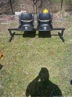 Photo of black two-seater waiting area chairs on grass, showing front and side view with rust and wear visible.