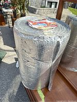 Full view of the reflective insulation roll standing vertically with visible textured double bubble foil surface and some damage on the outer foil layer.