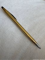 Gold colored twist pen lying on white background showing entire pen and tip side.