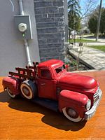 Side view of red metal display pickup truck showing wooden stake side railings and spare tire.