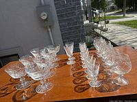 Photo of all assorted crystal stemware glasses arranged in rows on wooden surface outdoors, showing variety and cut pattern details.