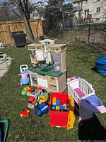 Step 2 plastic kitchen and assortment of kids toys including toy vehicles, Duplo blocks, and push scooters shown outside on grass.