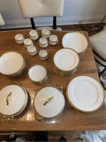 Full view of porcelain Limoges china set arranged on table showing coffee cups, plates in various sizes, serving bowls with lids including the chipped one.