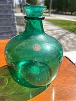 Emerald green blown glass vase shown in natural light, highlighting its color and glass texture with a round base and flared rim.