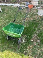 Shows the full Scotts Standard broadcast spreader with green hopper on two wheels, black handle, standing on grass.