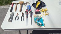 Wide view of all hand tools arranged on white table showing variety of hammers, pliers, screwdrivers, keychain hex sets, stud finder, soldering iron, and other tools.