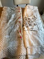 Two folded vintage large tablecloths on wooden surface, showing lace and floral needlepoint detail.