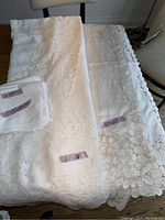 Two vintage white rectangular tablecloths laid out with lace and floral embroidery visible, including measurement tags.
