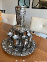 Front view of the wine decanter and kiddush cup dispenser set with 8 small cups arranged around the base.