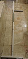 Full view of the white and gray adjustable support pole laid flat on the floor. The horizontal grip handle is visible along the top section of the pole. The pole shows a locking adjustable section near the middle.